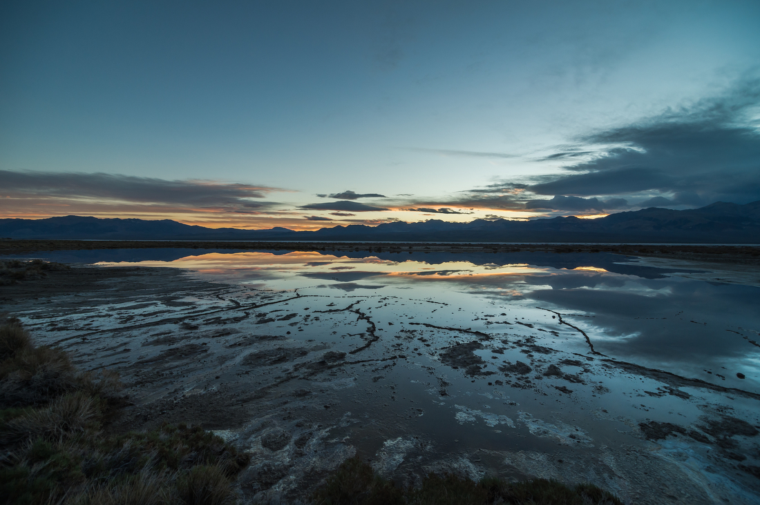 Shallow water reflecting the sky and surrounding mountains at Badwater Basin in Death Valley National Park at dusk